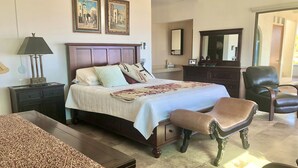 A bedroom with a bed, a nightstand, a lamp, a chair, a dresser, and two framed pictures on the wall.