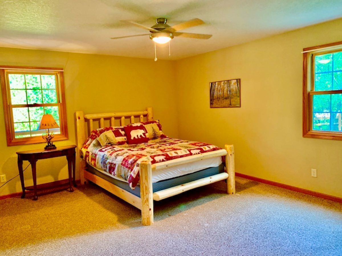 A bedroom with a wooden bed, a nightstand, a lamp, and a ceiling fan.