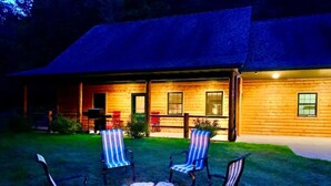 A log cabin with a fire pit and striped chairs in the yard. - Log Cabin/ w hot tub, outdoor pool & pool table (Lansing)