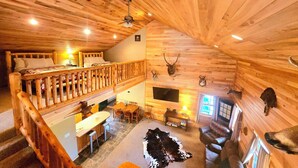 A log cabin interior with a loft bedroom, dining area, and a living room featuring mounted animal heads. - Log Cabin/ w hot tub, outdoor pool & pool table (Lansing)