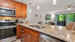A modern kitchen with wooden cabinets, stainless steel appliances, a granite countertop, and pendant lighting. - Tropical Kihei Resort, 3 Min Walk to Beach, A/C in All Rooms (Kihei)