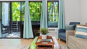A living room with a sofa, a coffee table with a plant, and a sliding glass door leading to an outdoor area with a chair and a table. - Tropical Kihei Resort, 3 Min Walk to Beach, A/C in All Rooms (Kihei)