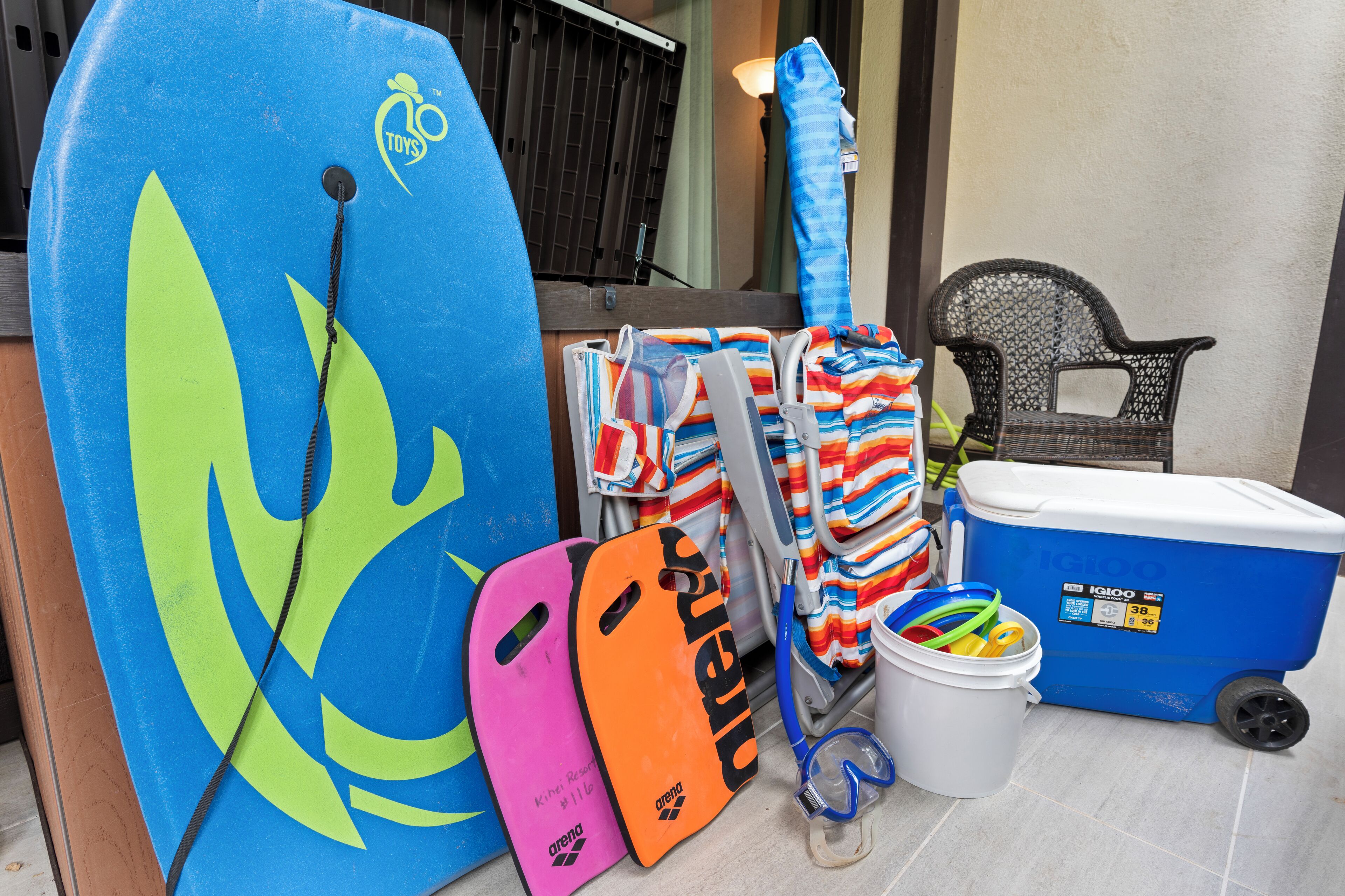 Un espacio de almacenamiento con tablas de surf, un enfriador y una silla.