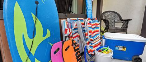 Un espacio de almacenamiento con tablas de surf, un enfriador y una silla.