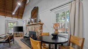A cozy living room with a fireplace, a round dining table, and comfortable seating. - Corner Cabin • AC • Spa • Game room • Dog Friendly (Big Bear)