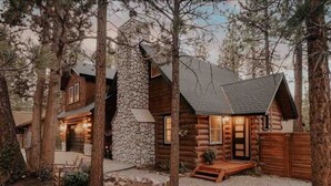 Une cabane en rondins avec une cheminée en pierre, un revêtement extérieur en bois et une véranda avec un banc.
