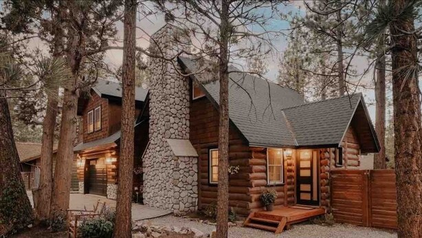 A log cabin with a stone chimney, wooden exterior, and a porch with a bench. - Corner Cabin • AC • Spa • Game room • Dog Friendly (Big Bear)