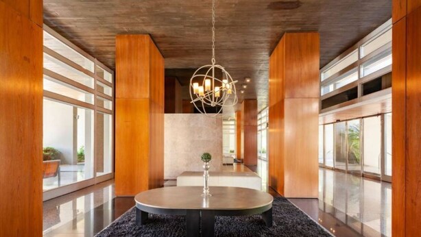 A modern lobby with a round table, a hanging light fixture, and large windows.