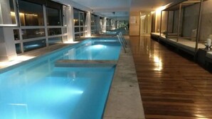 A swimming pool with a wooden deck and glass walls.
