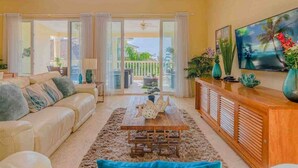 A living room with a sofa, coffee table, TV, and a balcony with sliding doors. - Beachfront residence in central Sosua, 2BD/2BTH with sea views. Chica-friendly! (Sosúa)