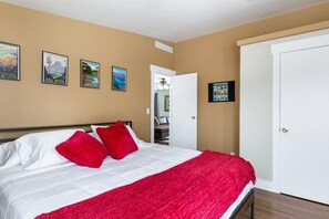 A bedroom with a bed, red pillows, a red blanket, and wall art.