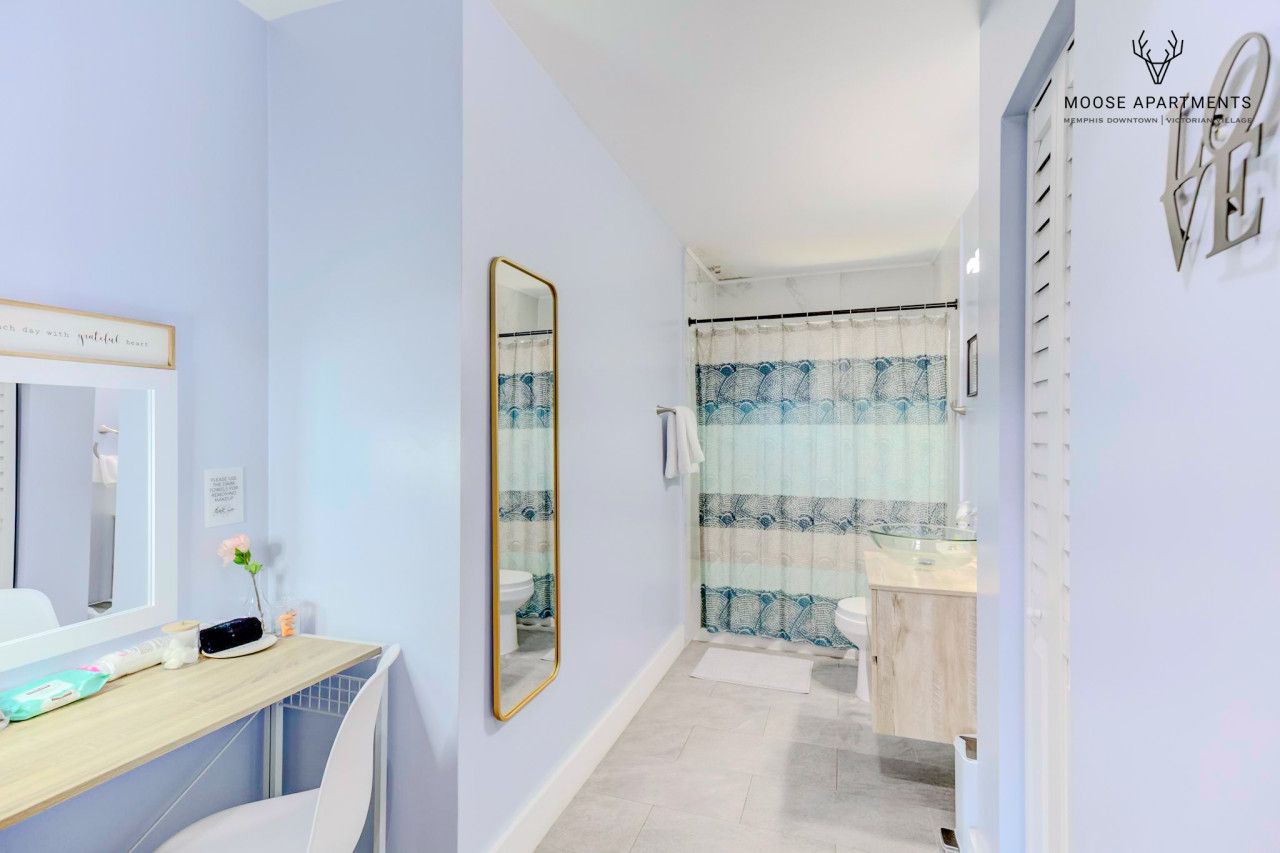 Un baño moderno con tocador, un espejo grande y una zona de ducha con cortinas estampadas.