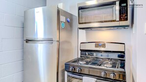 Een compacte keuken met een roestvrijstalen koelkast, een magnetron en een gasfornuis.