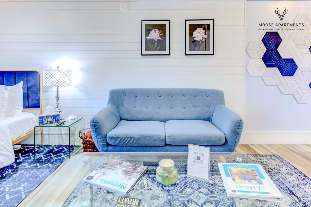 Una sala de estar moderna con un sofá azul, una mesa de centro de vidrio y obras de arte enmarcadas en la pared.