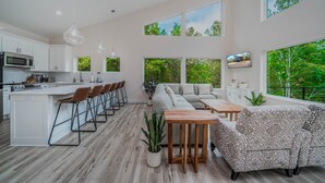 Eine moderne Küche mit weißen Schränken, einer zentralen Kochinsel mit Barhocker und einem Essbereich mit Sofa und Couchtisch.