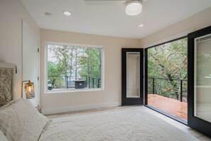 Une chambre avec une grande fenêtre, un balcon et un lit doté d’une tête de lit.