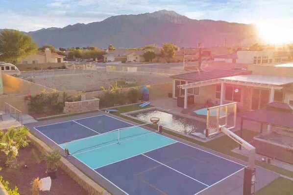 A tennis court with a water feature, surrounded by buildings and mountains in the background.