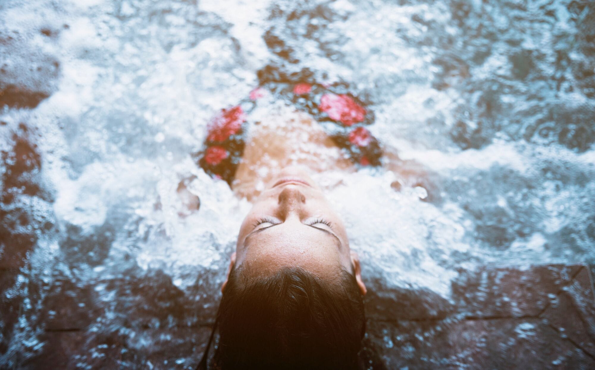 Eine Person ist im Wasser, vermutlich in einem Pool oder Whirlpool, wobei der Fokus auf der Wasseroberfläche und den Blasen liegt.