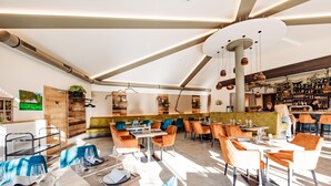 Un restaurante moderno con varias mesas y sillas, una zona de bar y diversos elementos decorativos y plantas.