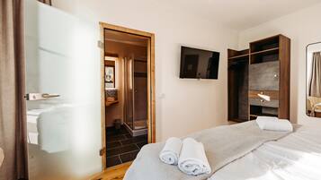 A hotel room with a bed, a TV mounted on the wall, a wooden wardrobe, and a shower area.