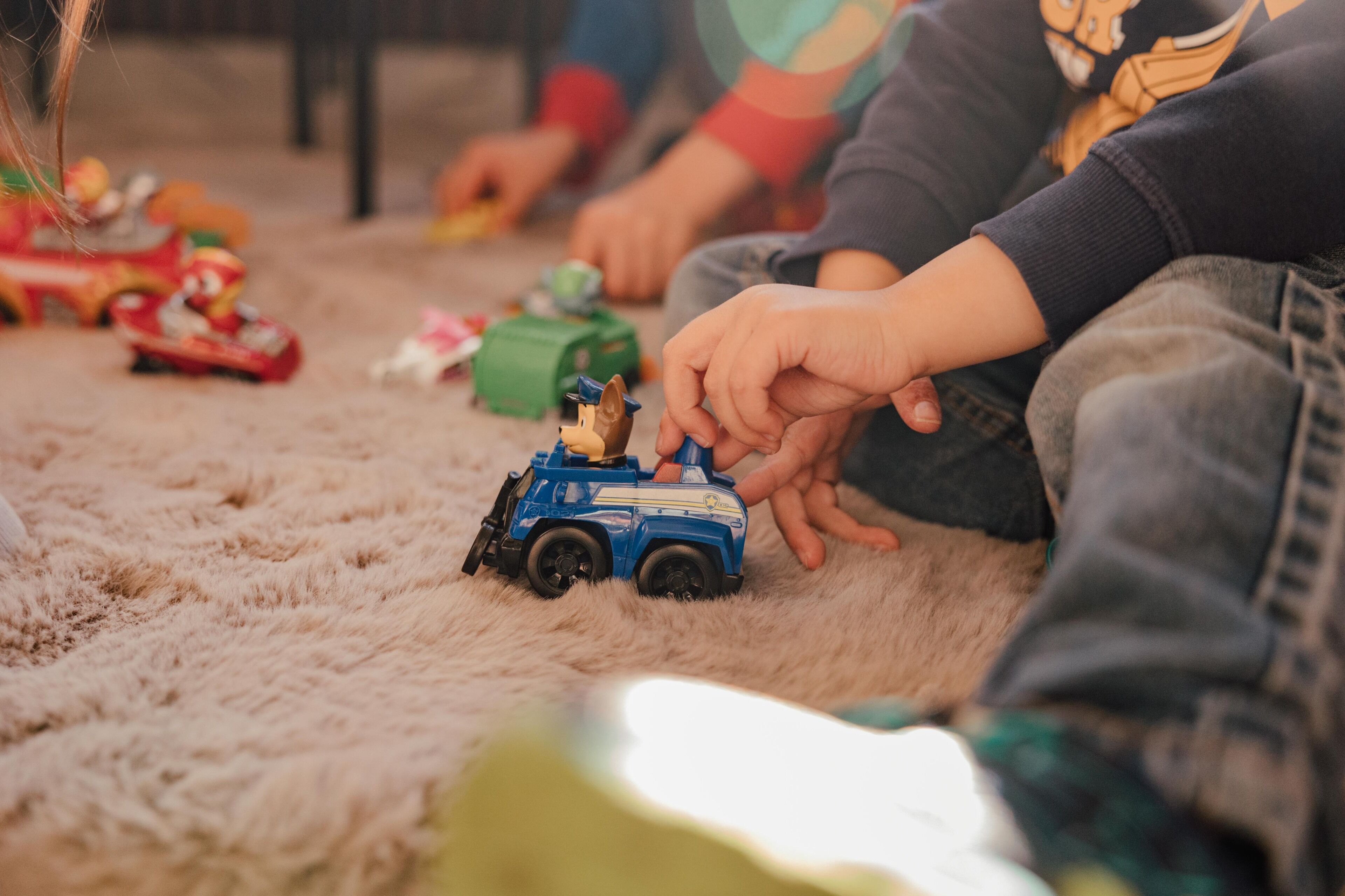 Children playing with toy vehicles on a carpeted floor.