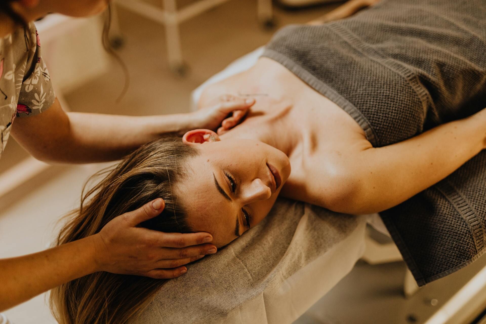 A person lying on a bed with a blanket, receiving a massage.