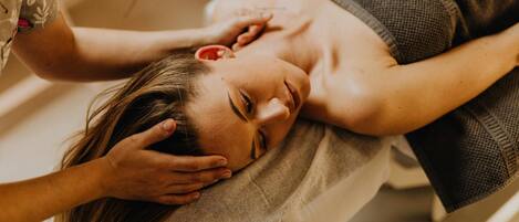 A person lying on a bed with a blanket, receiving a massage.
