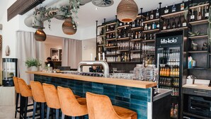 Una zona de bar con una barra larga, varios taburetes y estantes llenos de botellas y copas.