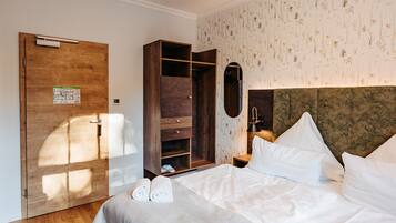 A hotel room with a wooden wardrobe, a bed with white linens, and a floral wallpaper pattern.