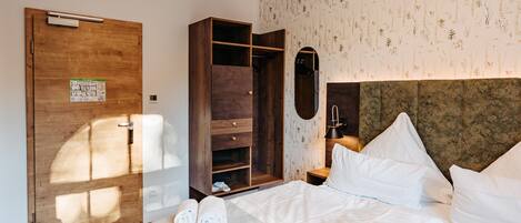 A hotel room with a wooden wardrobe, a bed with white linens, and a floral wallpaper pattern.