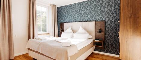 A bedroom with a large bed, a nightstand, a wardrobe, and a window with curtains.