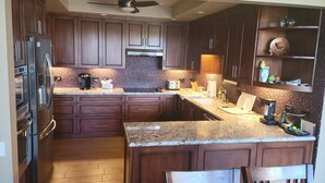 Una cocina con armarios de madera oscura, electrodomésticos de acero inoxidable, encimera de granito y ventilador de techo.