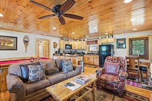 A spacious living room with a pool table, a sofa, a coffee table, and a patterned armchair.