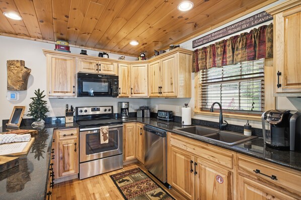 A modern kitchen with wooden cabinets, stainless steel appliances, and a large window with curtains.