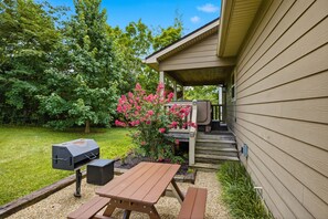 A patio area with a grill, a wooden table, and a bench.