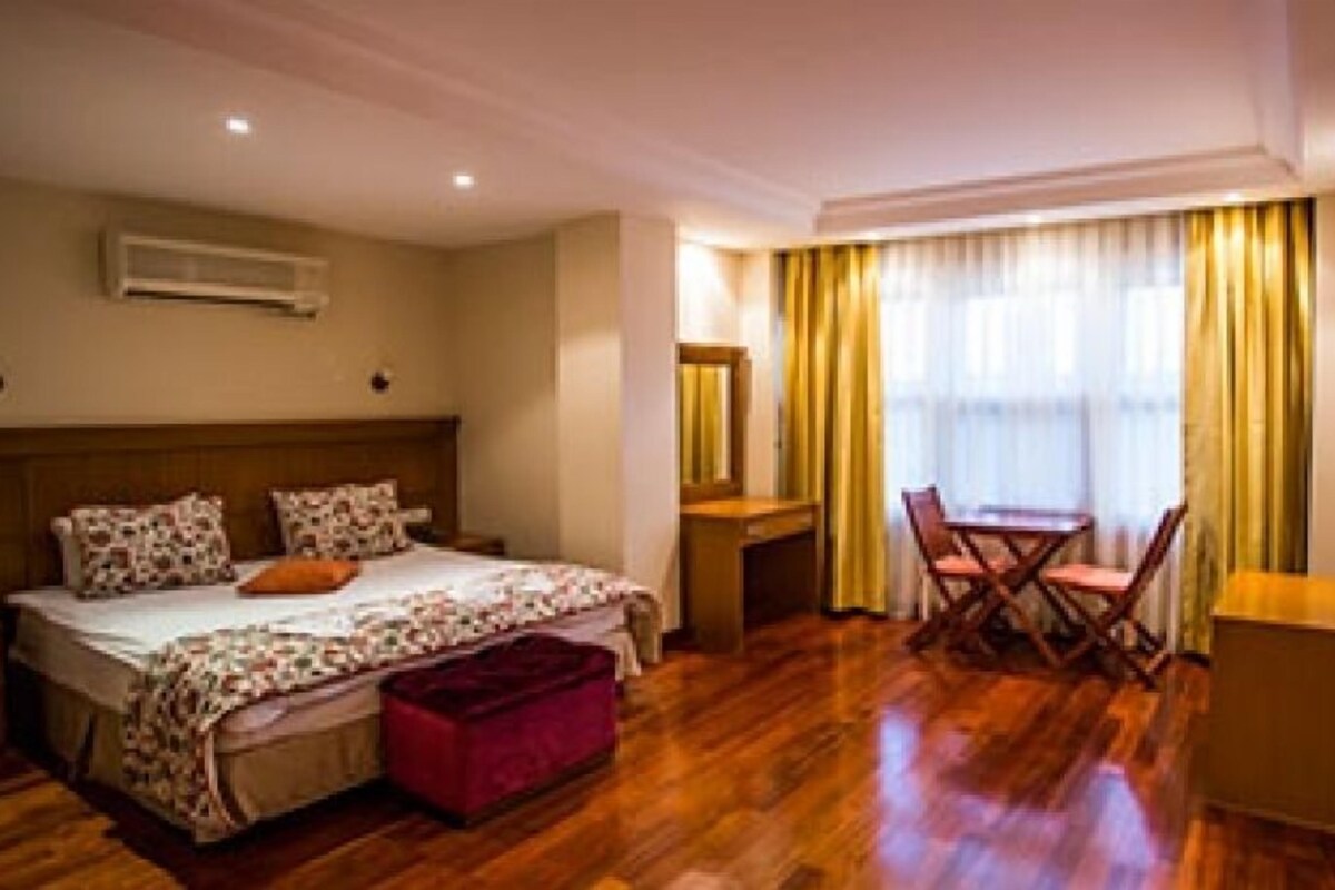 A hotel room with a bed, a desk, a chair, and a small table.