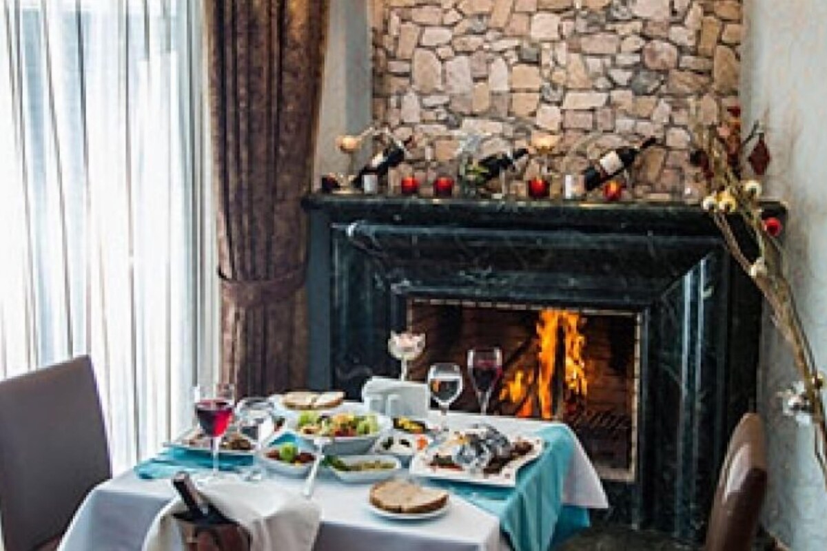 A dining area with a stone fireplace, a table set with plates of food, glasses, and a bottle of wine.