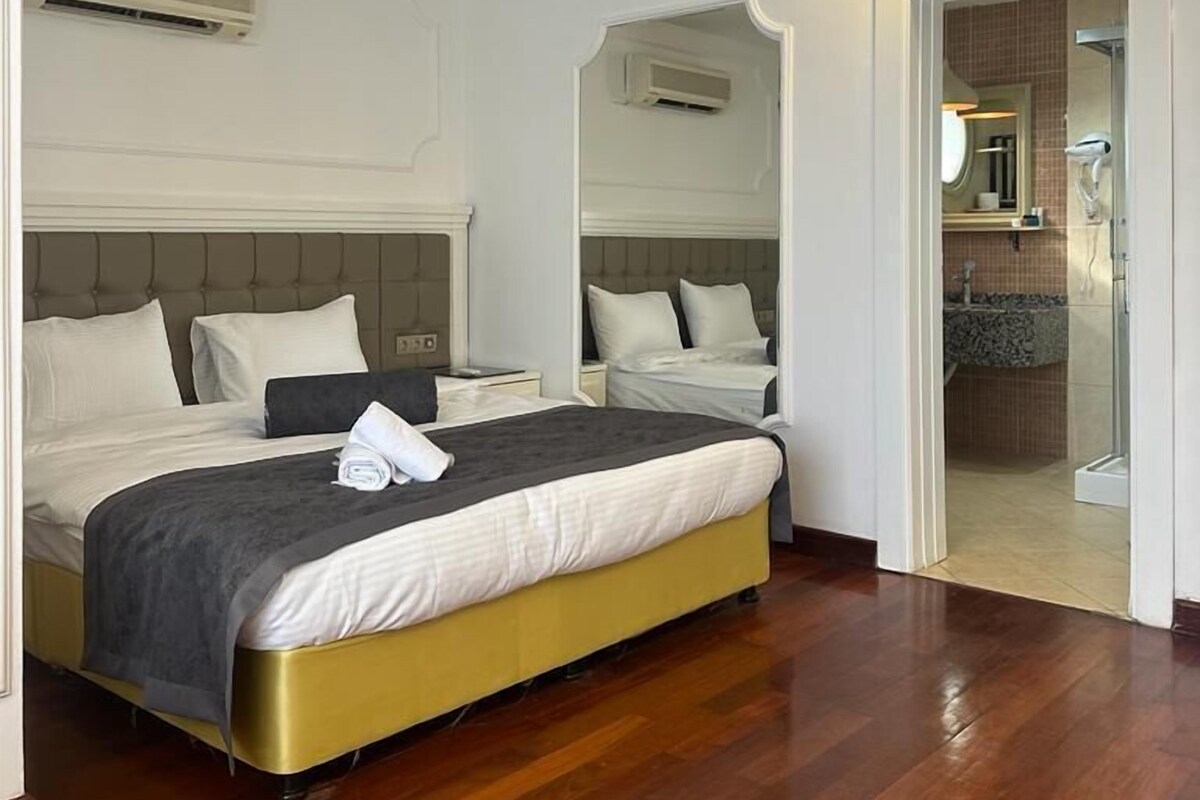 A hotel room with a large bed, a bedside table, and a mirror. There is a bathroom visible through an open door.
