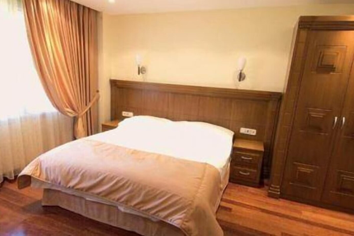 A hotel room with a large bed, wooden headboard, bedside tables, and a wardrobe.