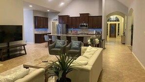A spacious living area with a large TV, comfortable seating, a kitchen with dark cabinets, and a decorative archway. - Luxury 1 story 3,272 SF. 12 miles from IAH airport (Houston)