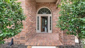 A brick building with a central arched doorway, surrounded by greenery. - Luxury 1 story 3,272 SF. 12 miles from IAH airport (Houston)
