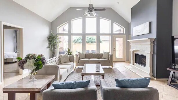 A spacious living room with a high ceiling, a fireplace, and a large window providing natural light. - Luxury 1 story 3,272 SF. 12 miles from IAH airport (Houston)
