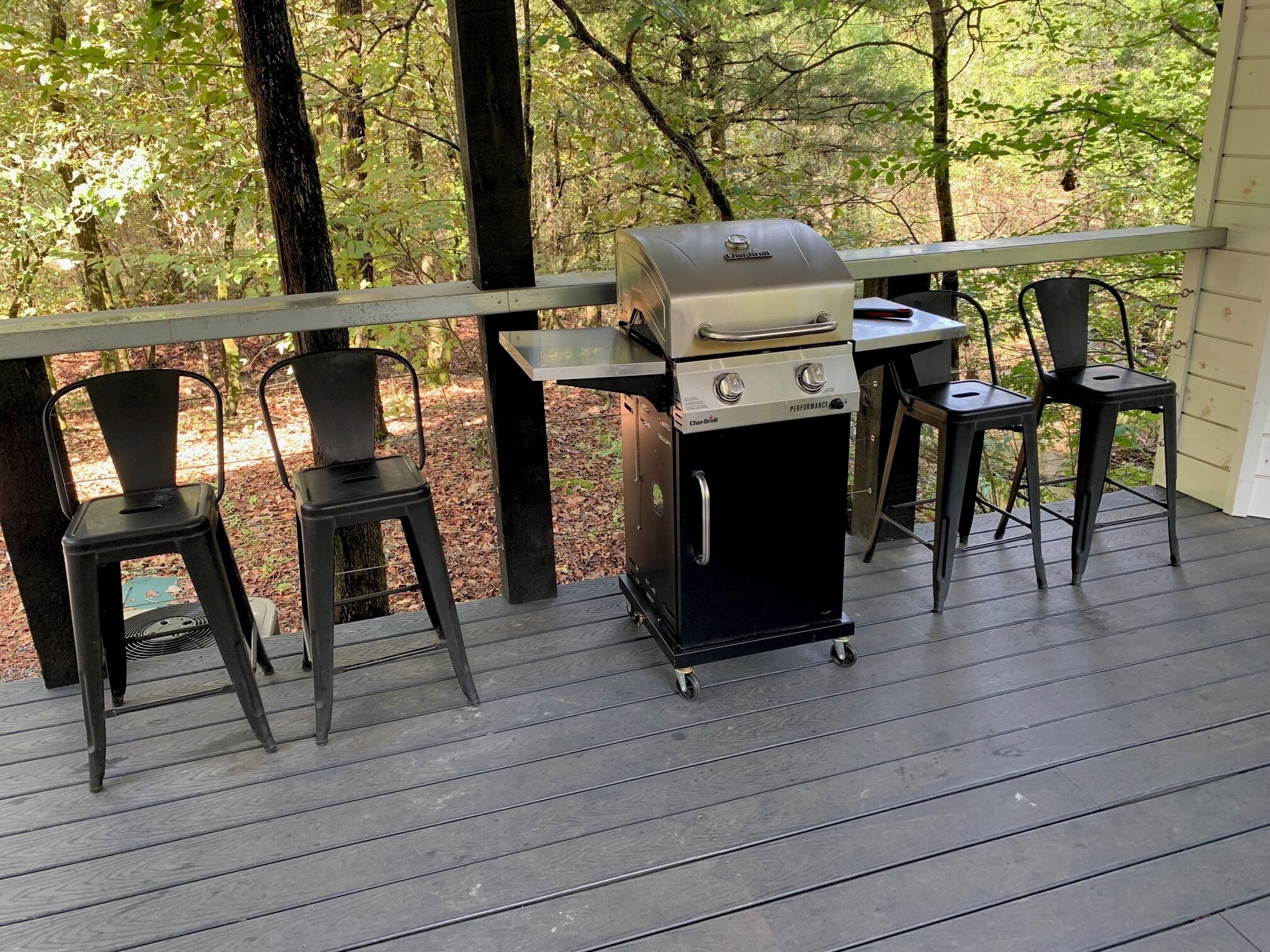 A deck with a Char-Bri grill, two metal chairs, and a table.