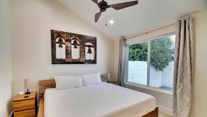 A bedroom with a large bed, a nightstand, a ceiling fan, a window with curtains, and a wall-mounted artwork. - Gilbert Ranch Retreat & Non Heated Pool. Walk to Shops and Restaurants. (Gilbert)