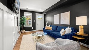 Ein modernes Wohnzimmer mit einem blauen Sofa, einem Glastisch und einem grauen Sessel.