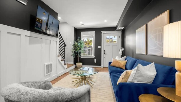 Ein modernes Wohnzimmer mit einem blauen Sofa, einem Marmor-Sessel, einem Glastisch und einer Treppe, die in einen anderen Raum führt.