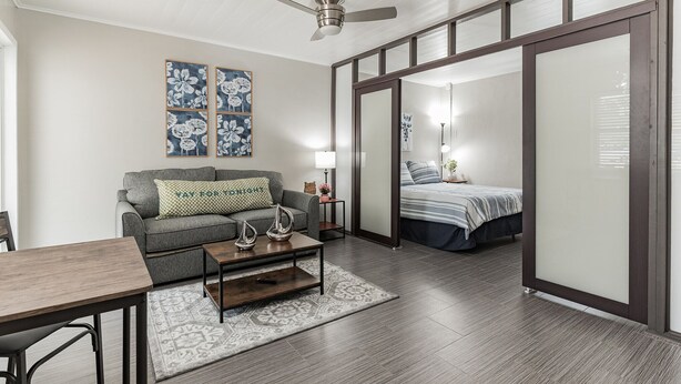 Uma sala moderna com um sofá, mesa de centro e uma cama no quarto adjacente.