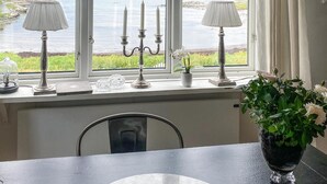 A dining area with a view of a lake, a table with a vase of flowers, and a window with decorative items. - 3 bedroom awesome home in Vallda (Vallda)