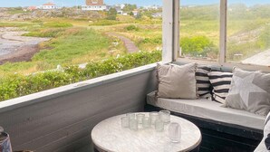 A balcony with a view of a coastal landscape, a seating area with cushions, and a small round table with glasses. - 3 bedroom awesome home in Vallda (Vallda)