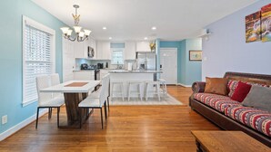Una cocina moderna con armarios blancos, una isla central y un comedor con mesa y sillas blancas.